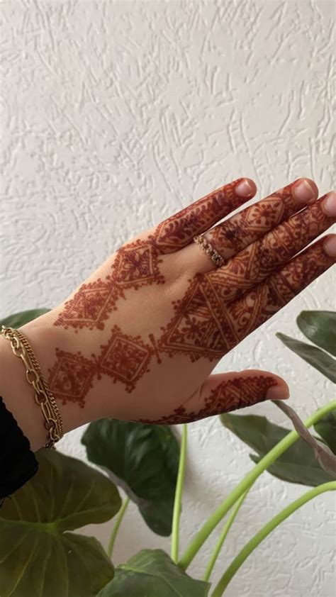 A Woman S Hand With Henna On It And Green Plants In The Background