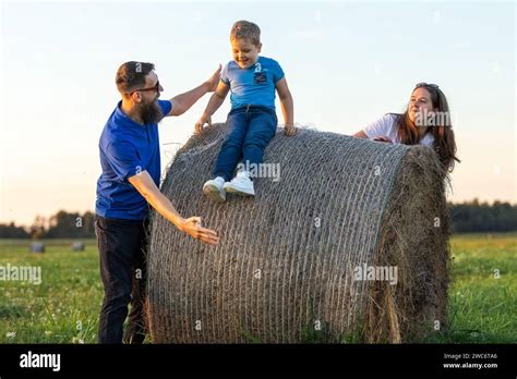 A Cheerful Little Boy Slides Down A Round Hay Bale His Father Tries To