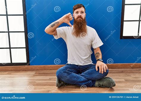 Redhead Man With Long Beard Sitting On The Floor At Empty Room Looking