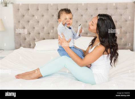 Happy Brunette Holding Her Baby Who Is Holding Smartphone Stock Photo Alamy