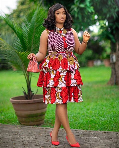 A Woman In A Red And White Dress Is Holding A Pink Purse While Standing