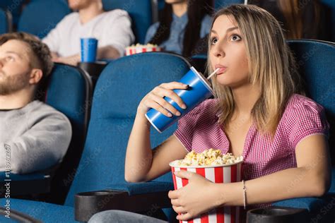 Movie night. Beautiful young female drinking and eating popcorn watching movies at the local ...