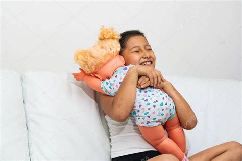 chica morena latina muy feliz abrazando a su muñeca mientras juega que ella es su hija la