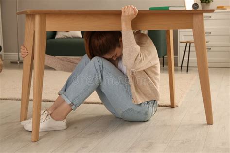 Scared Mother With Her Little Daughter Hiding Under Table In Living Room During Earthquake Stock