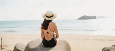 A Beautiful Brunette Woman Dressed In A Black Swimsuit And A Wide Brimmed Straw Hat Sits On