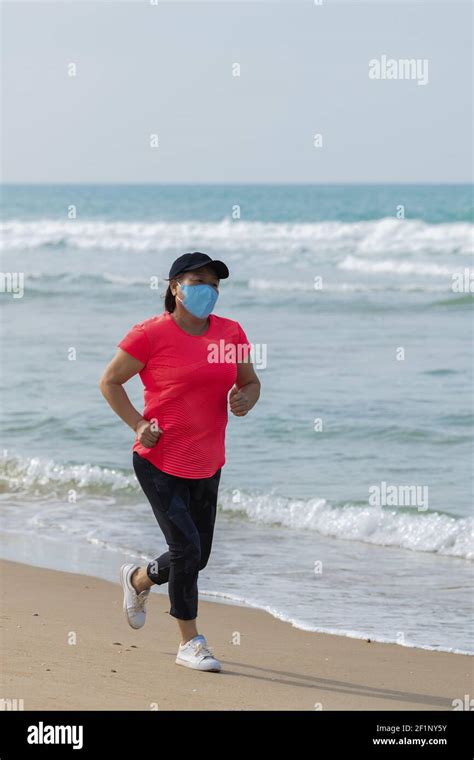 Mature Asian Woman Wearing A Face Mask Running On The Beach On An Out