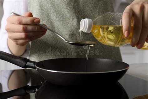 Woman With Spoon Pouring Cooking Oil Into Frying Pan On Stove Closeup