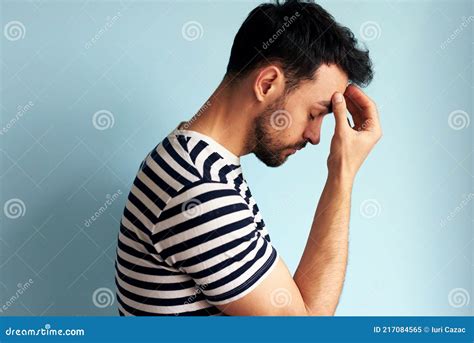 Side View Of A Tired Overworked Young Man Keeps Hand On Forehead With