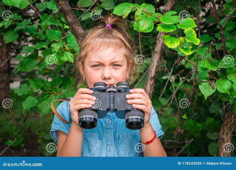 A Little Girl Holds Binoculars In Her Hands A Serious Child Observes