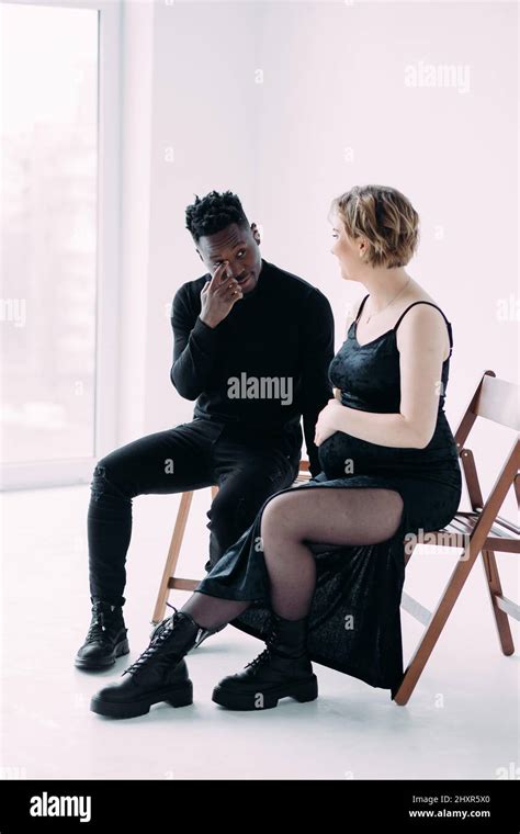 Young African Man And His Caucasian Pregnant Woman Sit On Chairs And