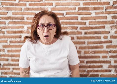 Senior Woman With Glasses Standing Over Bricks Wall Afraid And Shocked