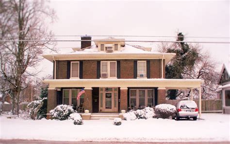 A Car Is Parked In Front Of A House With Snow On The Ground And Trees