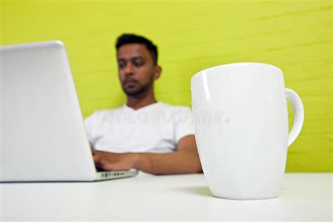 Indian Man Working At His Desktop With Mug In Focus In Foreground Stock