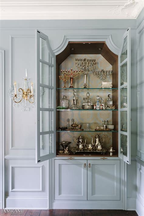 A White Cabinet With Glass Shelves And Chandelier In The Corner Between