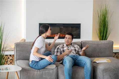 Brunette Male And Dark Haired Female Sitting On Sofa Arguing About