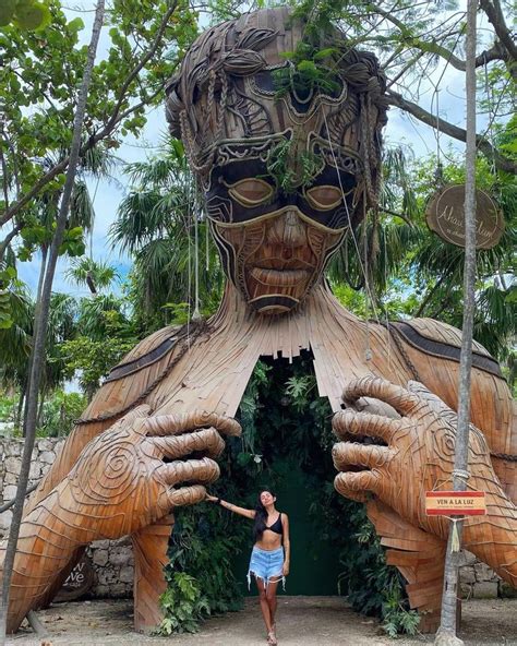 A Woman Standing In Front Of A Giant Wooden Statue