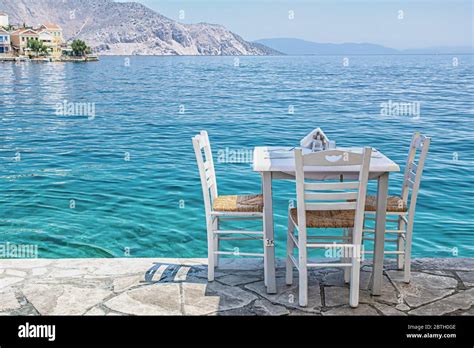 White Chairs With Tables In Typical Greek Tavern Near The Sea In Symi