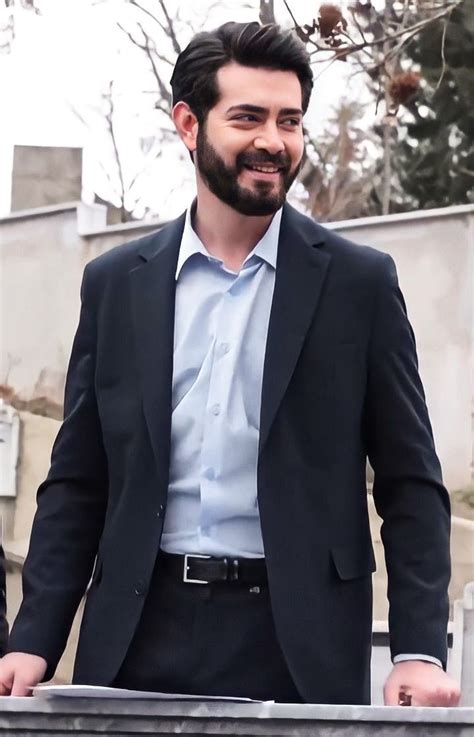 A Man Wearing A Suit And Tie Standing Next To A Fence With His Hands In