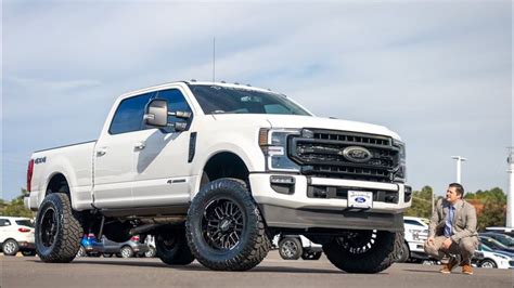 A White Truck Parked In A Parking Lot Next To Other Cars And People