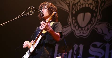 A Man With Glasses Playing Guitar In Front Of A Microphone