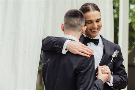 feliz pareja gay en trajes tomados de la mano y abrazos en el día de la boda