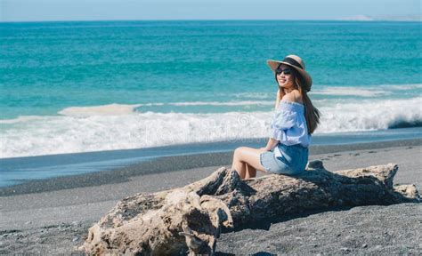 Portrait Of Pretty Asian Woman Sitting On The Trunk At The Black Sand