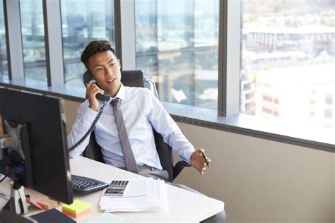 Businessman Making Phone Call Sitting At Desk In Office Stock Photo