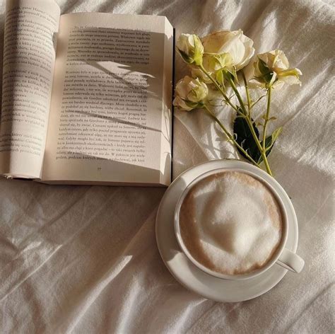 A Cup Of Coffee Next To An Open Book And Some Flowers On A White Sheet