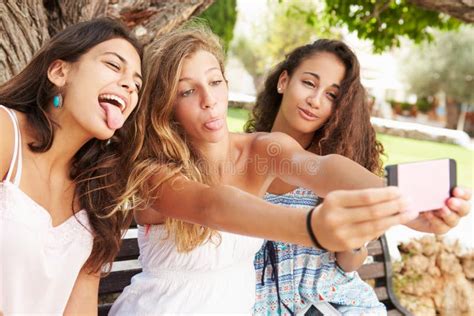 Trois Adolescentes S Asseyant Sur Le Banc Prenant Selfie En Parc Photo