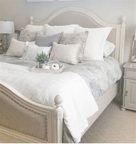 A White Bed Topped With Lots Of Pillows Next To A Night Stand And