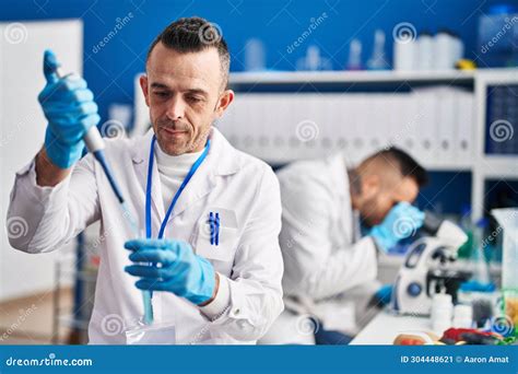 Two Men Scientists Pouring Liquid On Test Tube Using Microscope At