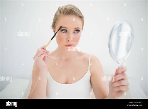 Natural Calm Blonde Holding Mirror And Using Eyebrow Brush Stock Photo