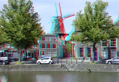 A 3d Image Of A Windmill In The Middle Of A Town With Cars Parked On