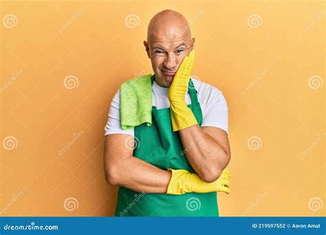 Middle Age Bald Man Wearing Apron Holding Cleaning Gloves Thinking