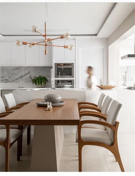 A Dining Room Table With Chairs Around It And A Woman In The Kitchen