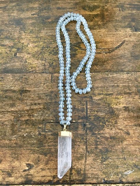 A Long Beaded Necklace With A Crystal Point Hanging From It S End On A