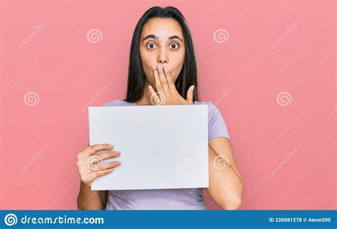 Young Hispanic Woman Holding Blank Empty Banner Covering Mouth With Hand Shocked And Afraid For