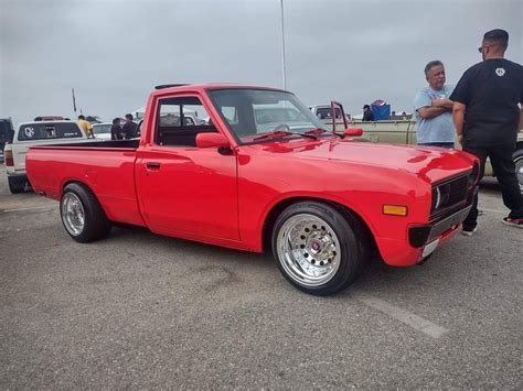 A Red Pick Up Truck Parked In A Parking Lot Next To Other Cars And People