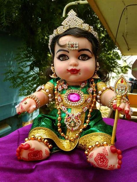 A Small Doll Sitting On Top Of A Purple Cloth Next To A Green And Gold