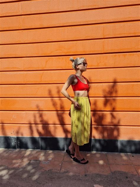 A Woman Standing In Front Of An Orange Wall With Her Hands On Her Hips