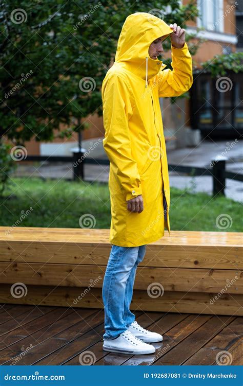 Man In Yellow Raincoat With The Hood Standing On Wet Wooden Floor In