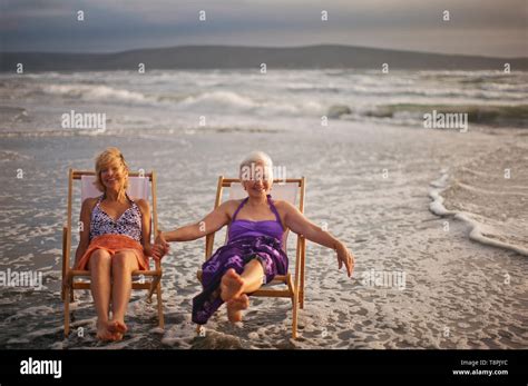 Two Happy Mature Women Relaxing In Deck Chairs On The Beach Stock Photo