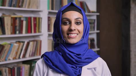 Young Happy Muslim Woman In Hijab Standing In Library And Looking At