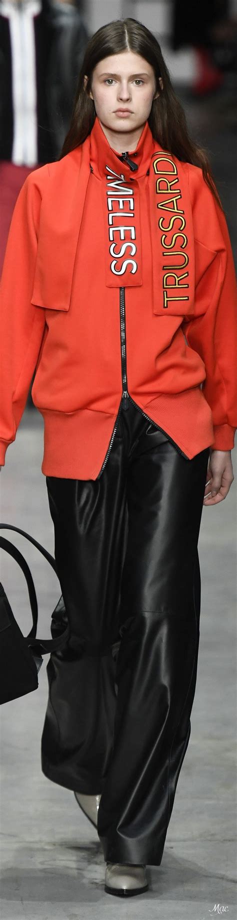 A Model Walks Down The Runway Wearing An Orange Jacket And Black Pants