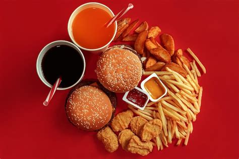 Two Hamburgers And French Fries Sauces And Drinks On Red Background