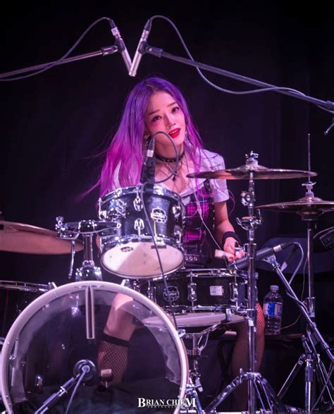 A Woman With Pink Hair Playing Drums On Stage