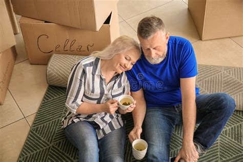 Mature Couple With Belongings Sitting On Carpet And Drinking Tea