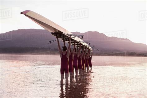 Rowing Team Carrying Row Boat Overhead In Still Lake Stock Photo