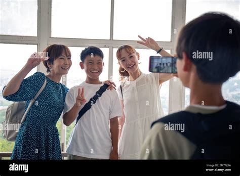 A Boy Using His Mobile Phone To Take A Picture Of Three Japanese People