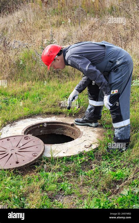 A Male Working Plumber In Overalls Shines A Flashlight Into A Water